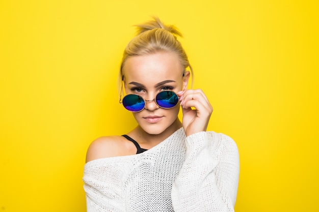 Free photo lovely blonde girl in modern white sweater in brilliant blue sunglasses is posing on yellow