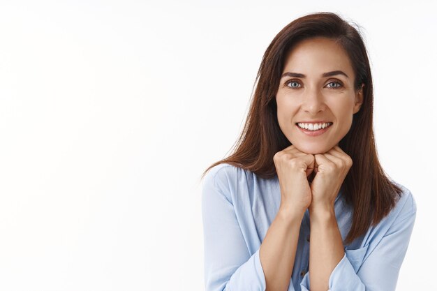 Lovely carefree lucky adult woman brunette with tattoo, lean hands looking joyful and happy at front, listen interesting story, gaze fascianted flirty, enjoy having good conversation, white wall