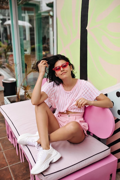 屋外カフェに座っているスニーカーで素敵な白人の女の子夏の日を楽しんでいるかわいい日焼けした女性