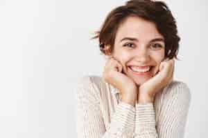 Foto gratuita bella donna caucasica viso magro sulle mani e sorridente felice in piedi sul muro bianco in camicetta casual