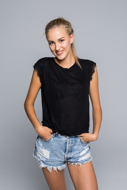 Lovely charming happy woman wears white t-shirt and denim shorts smiling at camera and touching her hair over isolated background