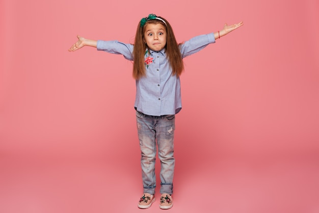 Lovely child girl in hair hoop and casual clothes giving huge hug with open hands while being isolated against pink wall