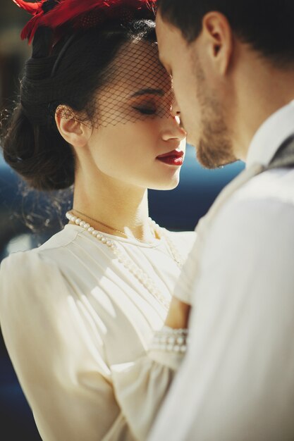 Lovely couple dressed in 30's style hugs on the street standing before an old car