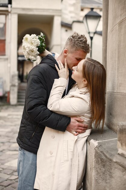 秋の時間に通りで抱き合ったりキスしたりする素敵なカップル旧市街の通りで花の花束を持っている男と女ベージュのコートと男の黒いジャケットを着ている女の子