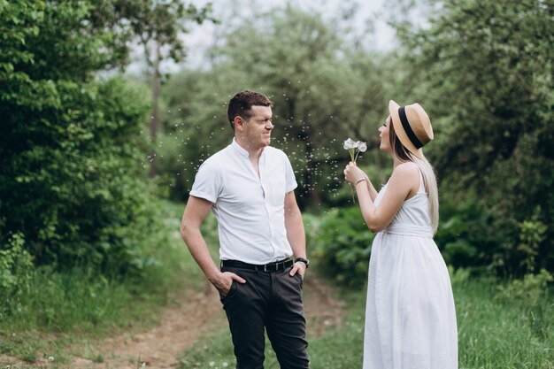 The lovely couple in love standing on the grass and blowing dandelions