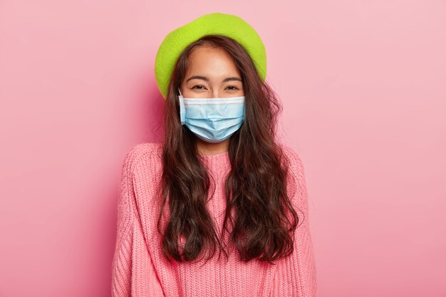 Lovely dark haired Asian lady has epidemic disease, wears protective medical mask, green beret and sweater