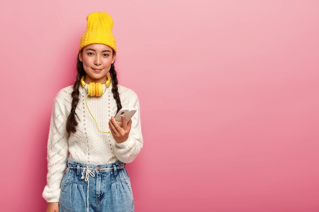 lovely eastern teenage girl uses headphones connected to mobile phone, listens music