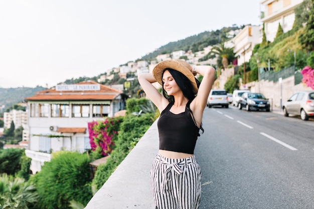 Lovely excited girl with dark hair enjoying freedom in beautiful european town during summer vacation