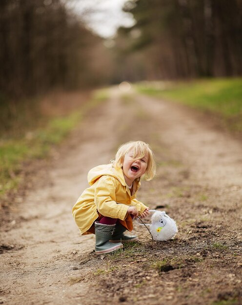 Lovely funny Dutch baby girl in a yellow waterproof coat and boots playing in the countryside field