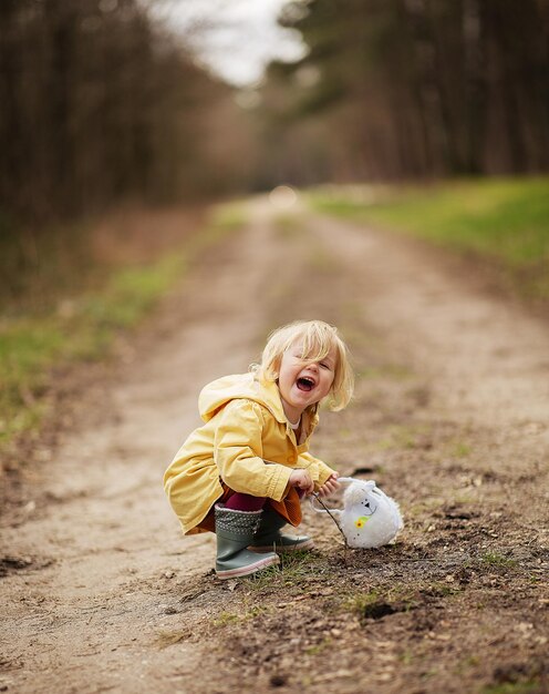 Милая забавная голландская девочка в желтом непромокаемом пальто и сапогах играет в сельской местности