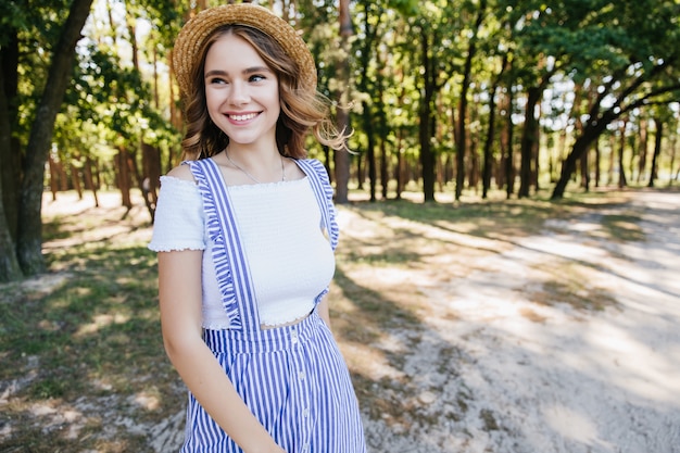 Lovely girl posing with happy face expression on forest. Carefree fair-haired woman having fun in summer weekend.