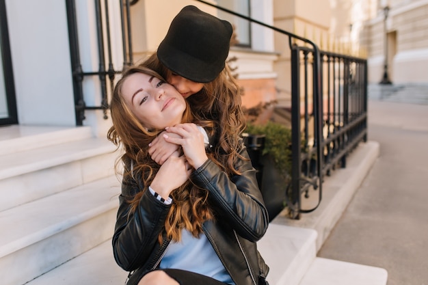 Lovely girl with beautiful brown long hair tightly embracing her joyful mother, touching her hands.