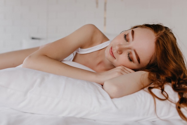 Free photo lovely girl with wavy hairstyle sleeping on pillow. indoor photo of tired ginger female model with makeup.