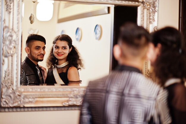 サリーで恋をしている素敵なインドのカップルとレストランでポーズをとったエレガントなスーツ両方が鏡を見る