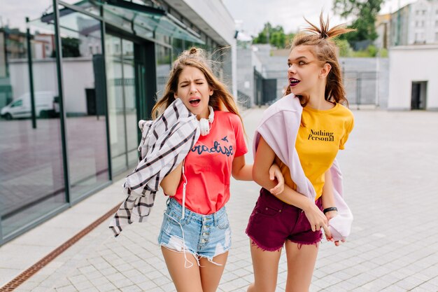 Милые радостные девушки в модной летней одежде гуляют по магазинам и обсуждают что-то интересное