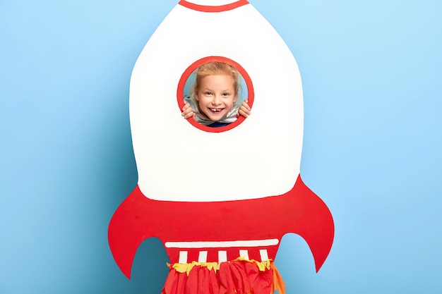 Lovely kid poses behind big paper rocket