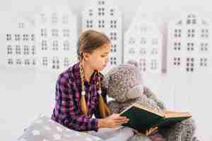 Бесплатное фото Милая маленькая девочка читает книгу с ее плюшевым мишкой