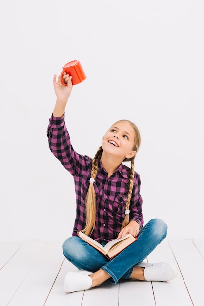 Lovely little girl reading a book and holding a mug