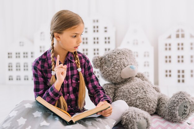 Lovely little girl reading a book with her teddy bear