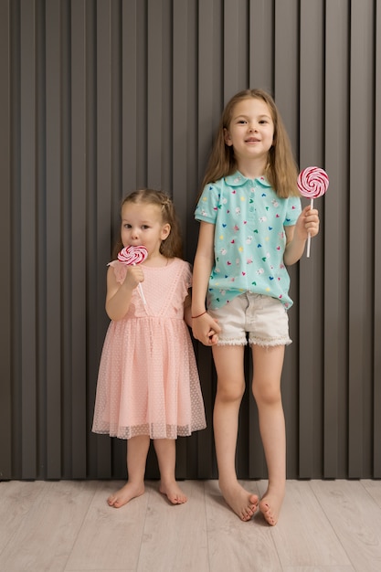 Lovely little girls with lollypop on gray background