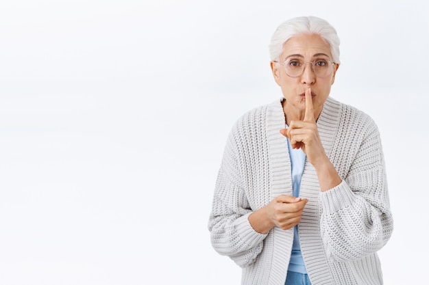 Free photo lovely senior lady have little secret, asking not tell anyone, prepare christmas surprise for husband. grandmother telling keep quiet showing hush gesture, press index finger to folded lips