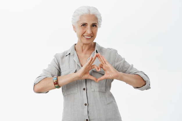 Donna maggiore sorridente adorabile che mostra gesto del cuore