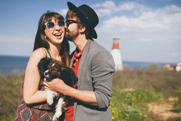 Lovely smiling young stylish hipster couple in love walking with dog in countryside