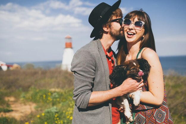 Lovely smiling young stylish hipster couple in love walking with dog in countryside