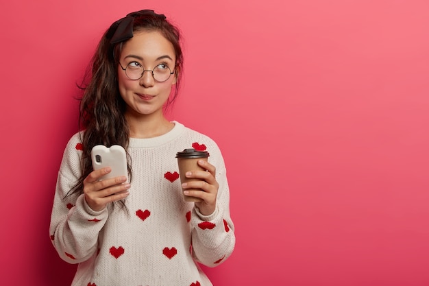 Una bella studentessa dall'aspetto orientale gode del tempo libero con caffè aromatico e gadget moderni, connessi a internet wireless