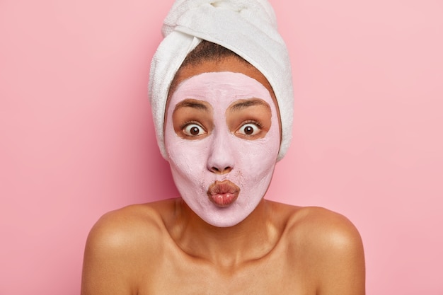 Free photo lovely surprised female model applies clay mask, keeps lips folded, wears white soft towel on white head, has daily beauty regime