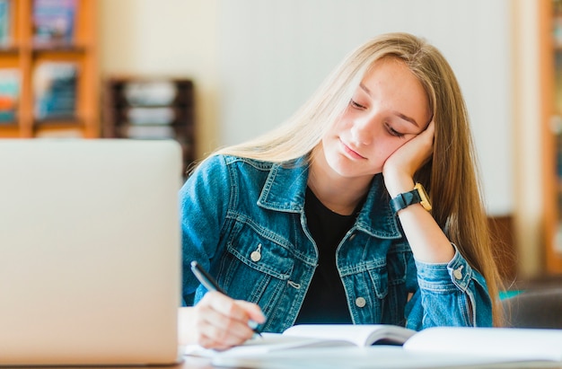 Lovely teenager making notes near laptop