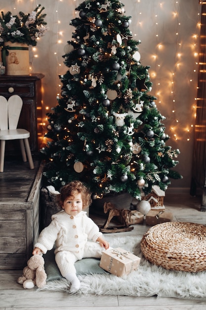 Adorabile bambino con un peluche e un regalo seduto sul tappeto vicino all'albero di natale