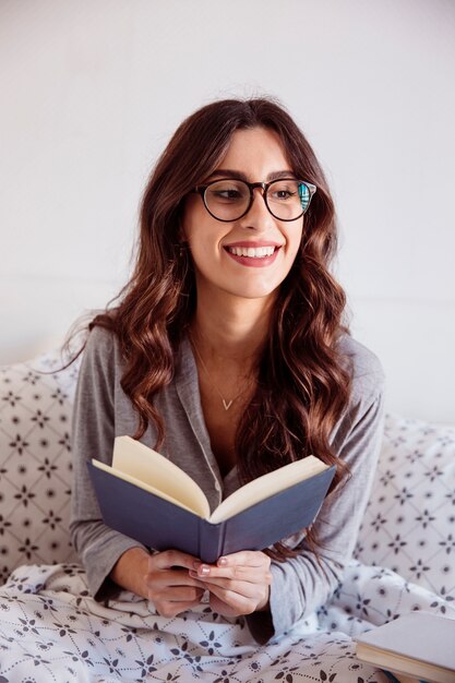 Lovely woman in glasses reading in bed