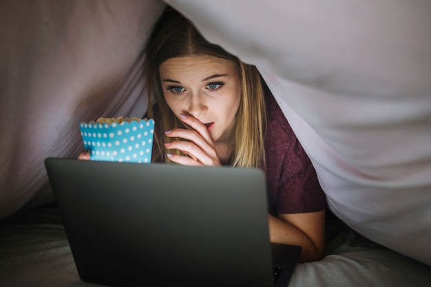 Lovely woman watching movie in blanket tent