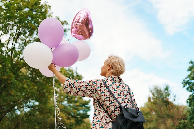 Прекрасная женщина с рюкзаком, ходьба счастлива с розовыми воздушными шарами в парке. Концепция свободы и здоровых женщин.
