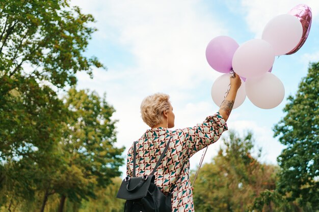Foto gratuita bella donna con lo zaino che cammina felice con palloncini rosa nel parco. libertà e concetto di donne sane.