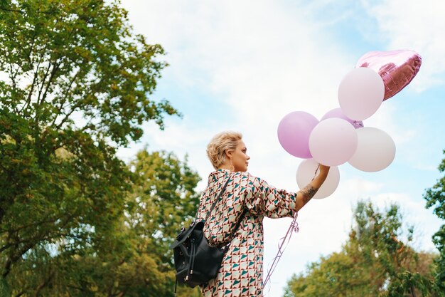 Прекрасная женщина с рюкзаком, ходьба счастлива с розовыми воздушными шарами в парке. Концепция свободы и здоровых женщин.