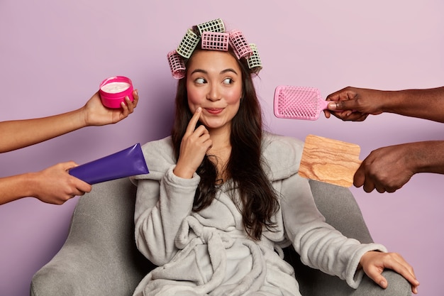 Free photo lovely woman with pensive dreamy expression, wears hair curlers and bathrobe