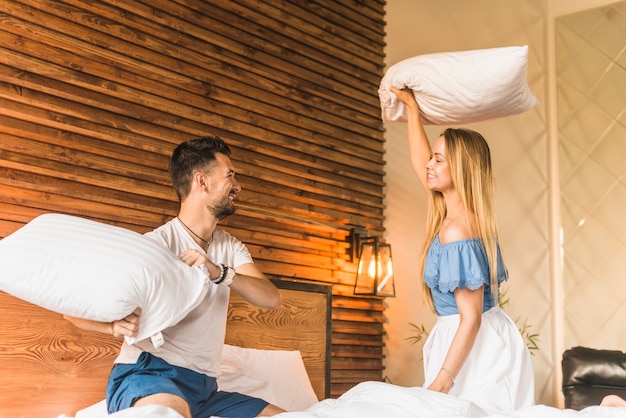 Free photo lovely young couple having pillow fight on bed