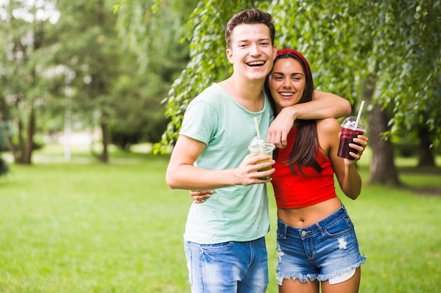 Free photo lovely young couple holding smoothies in plastic cup