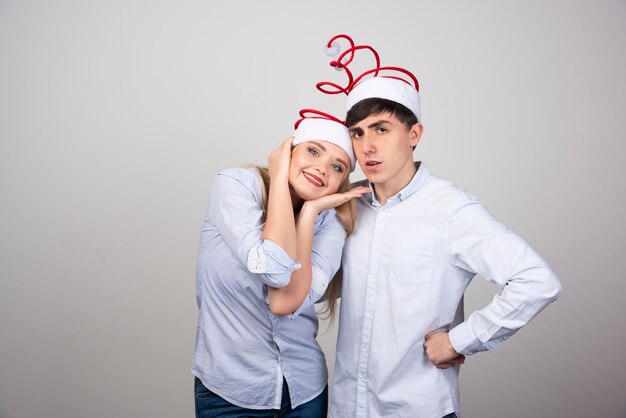 Lovely young couple standing in Santa hats on gray wall.