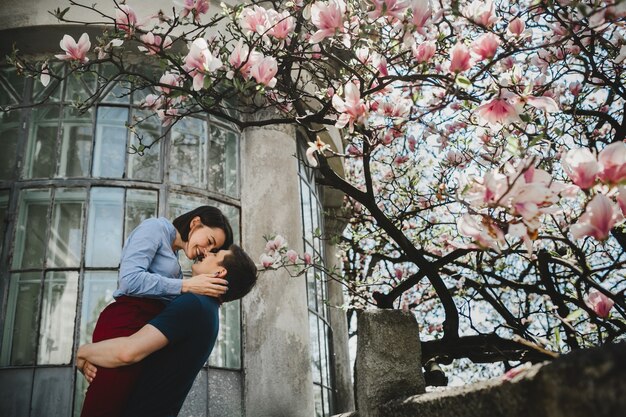 Lovely young couple stands under blooming tree outside and hug each other tender