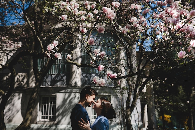 Lovely young couple stands under blooming tree outside and hug each other tender