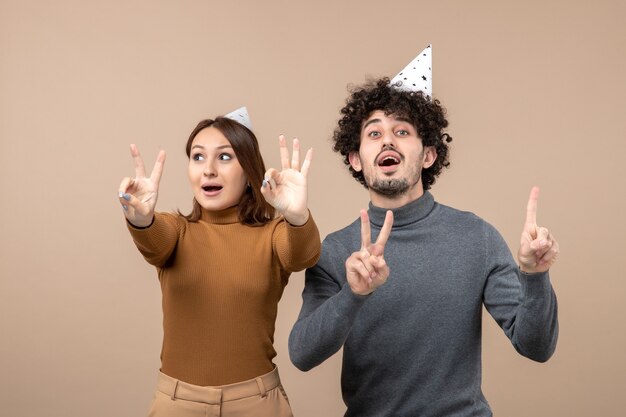 Free photo lovely young couple wear new year hat girl showing five guy showing three on gray