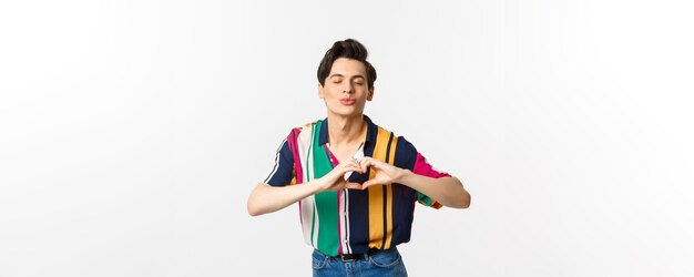 Lovely young man pucker lips and showing heart sign waiting for kiss I love you gesture standing over white background