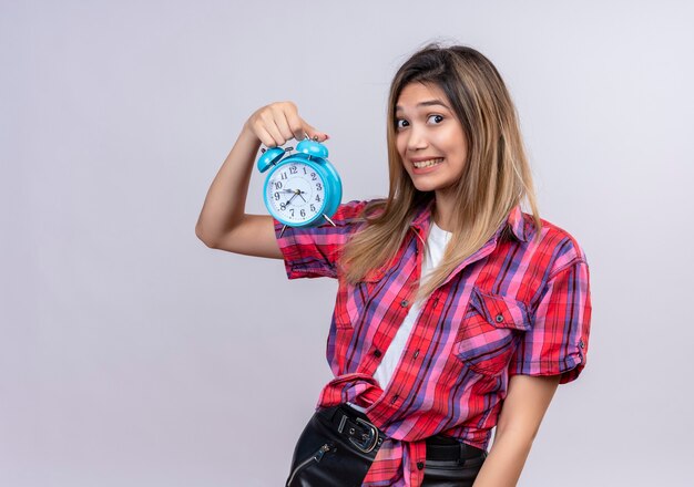 Una bella giovane donna in una camicia a quadri che mostra la sveglia blu