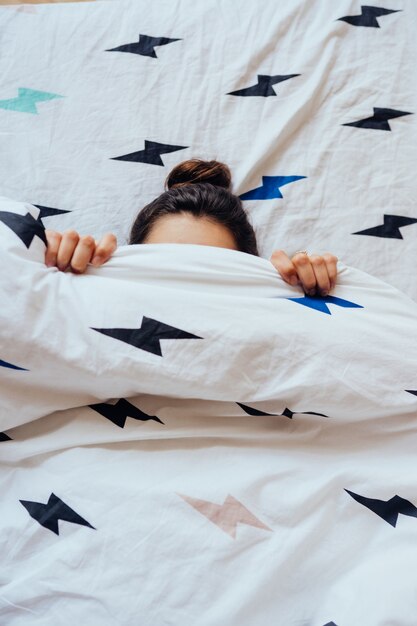 Lovely young woman lies in bed covered with blanket