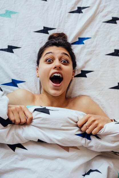 Lovely young woman lies in bed, covered with blanket