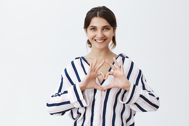 Lovely young woman showing heart gesture and smiling