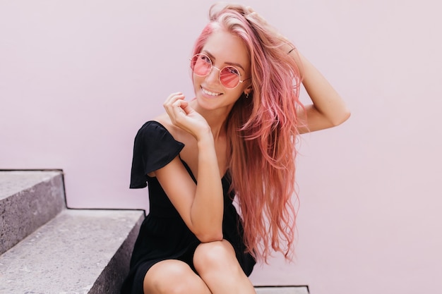 Lovely young woman with long hairstyle sitting on stairs and smiling.